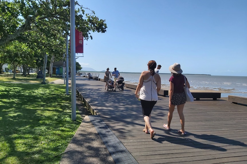 People stroll along the Cairns esplanade with blue skies and trees