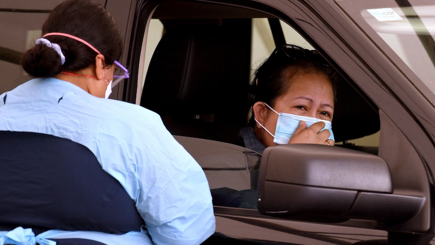A person in the front seat of a car waits a COVID test from a healthcare worker.