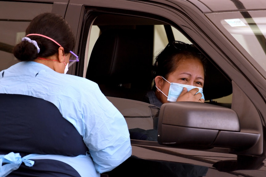 A person in the front seat of a car waits a COVID test from a healthcare worker.