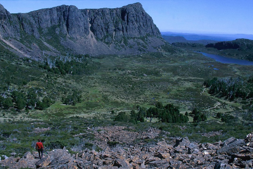 A view of a mountain landscape taken from a rocky outcrop overlooking green wilderness and a lake in the distance.