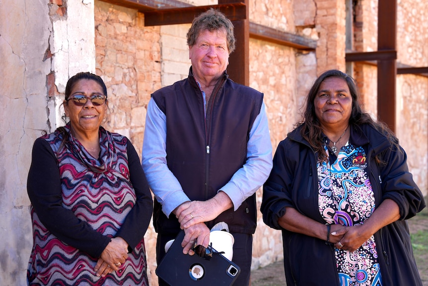 Two indigenous wilcannia residents standing next to a tall white man holding a hard hat. 