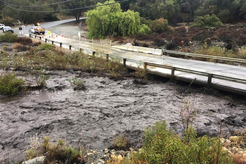 Flash flood water blackened by ash and debris flows under a bridge.