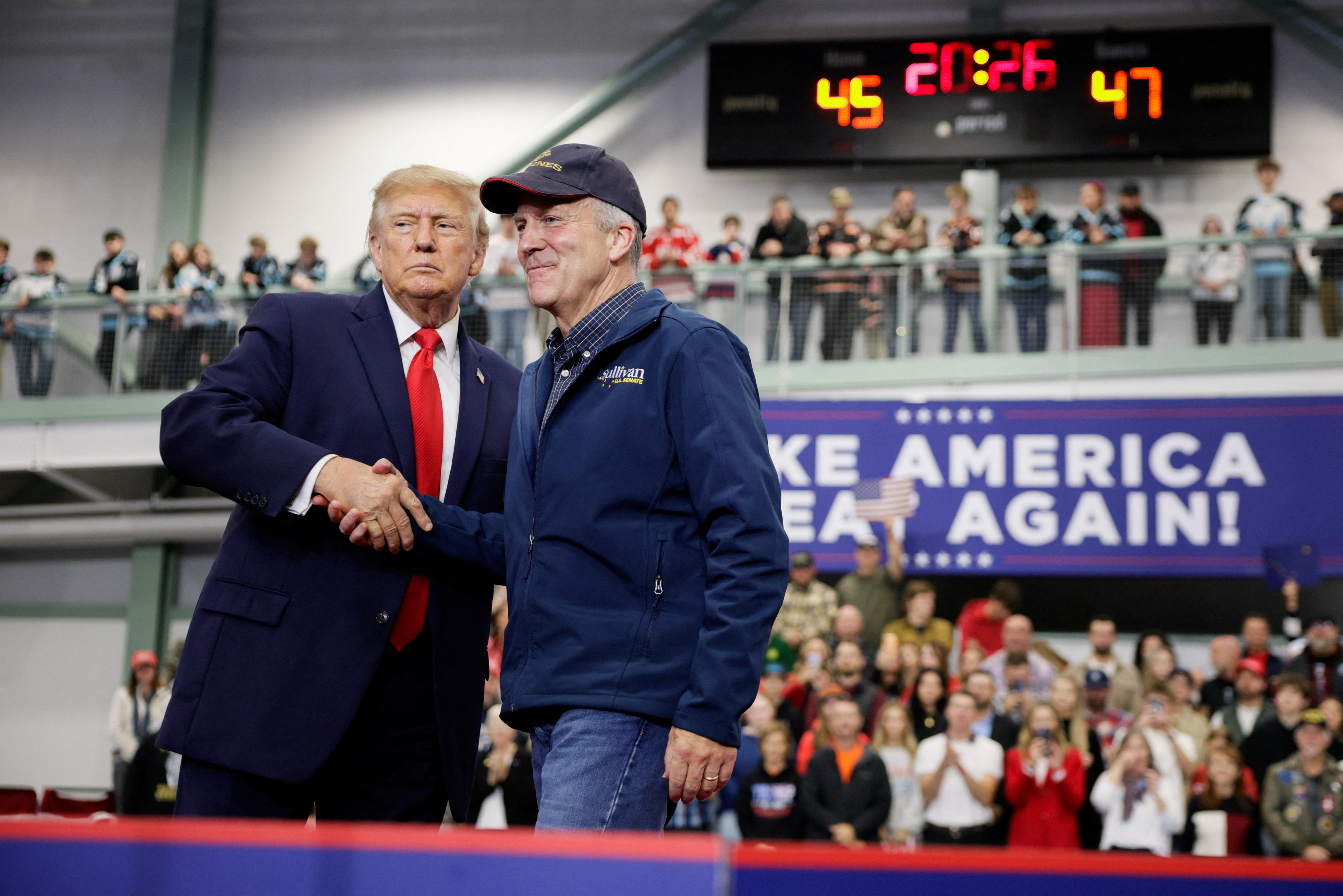 Donald Trump and Dan S Sullivan shake hands on a stage in Alaska.
