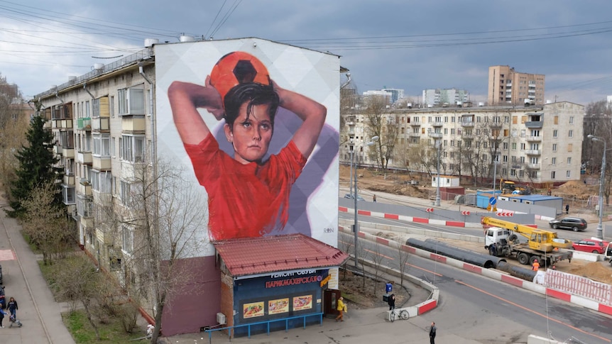 Picture of a boy on the side of a 5 story building in Moscow about to throw a soccer ball