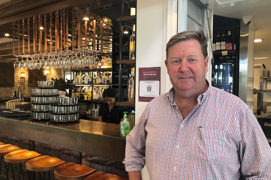 Man in button up shirt standing in front of cocktail bar