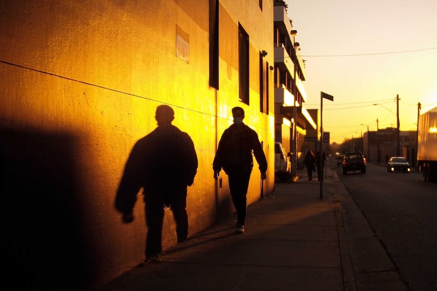 A man walks down a street at sunset and his shadow is cast against a wall.