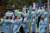 A large group of people waring blue gowns and face masks stands in front of a playground.