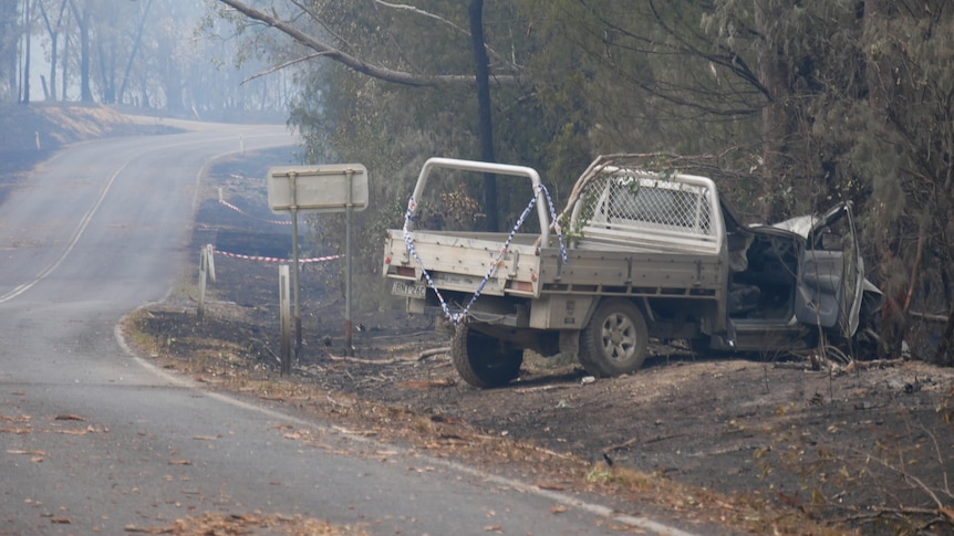 A ute in burnt out surroundings on the side of a road.