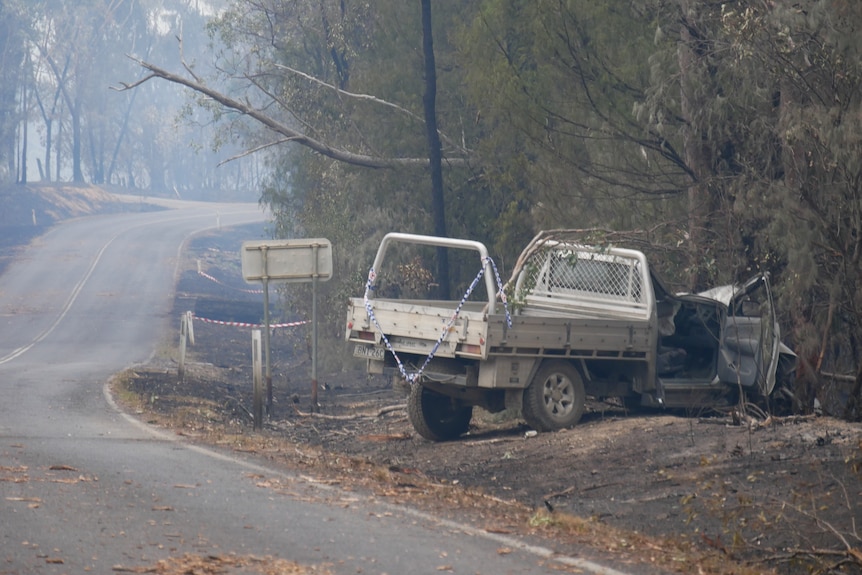 A ute in burnt out surroundings on the side of a road.