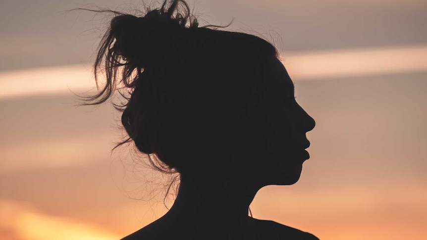 A woman's side profile in silhouette against a sunset.