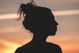 A woman's side profile in silhouette against a sunset.