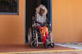 An elderly woman in a wheelchair with oxygen tank tubes on the ground.