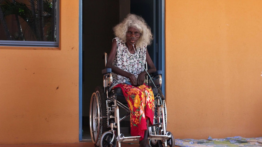 An elderly woman in a wheelchair with oxygen tank tubes on the ground.