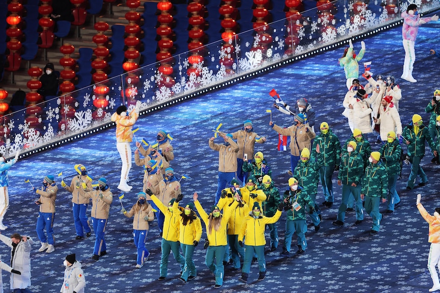 Un grupo de atletas olímpicos australianos saluda a la multitud mientras marchan con sus trajes verdes y dorados en la ceremonia de clausura.
