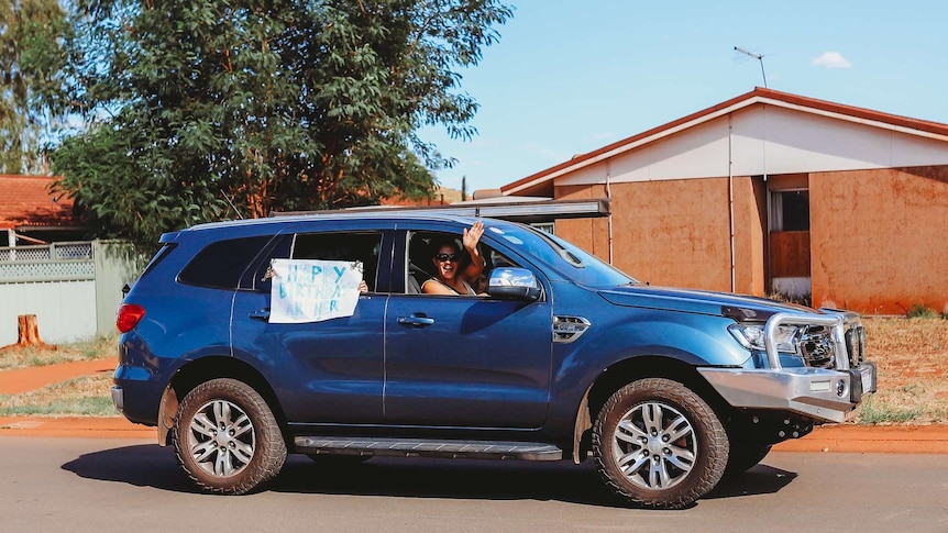 A four wheel drive with kids in the back seat holding home made birthday signs.