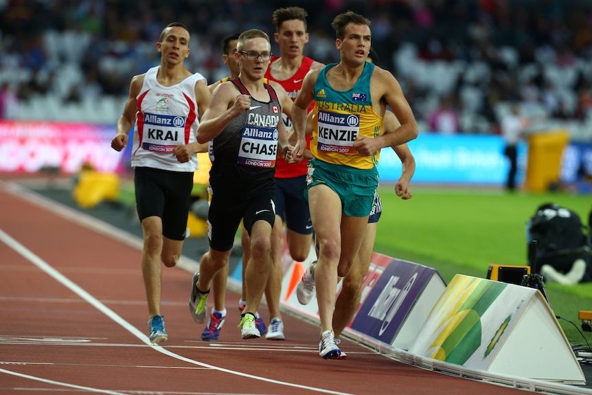 a man wearing green and gold running on a track in front of a group of men