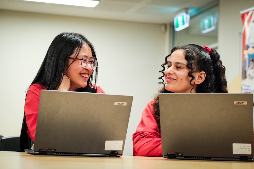 two young female students,one wearing glasses, talking and smiling