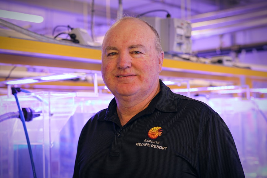 A man in a black polo shirt stands in a room full of scientific gear