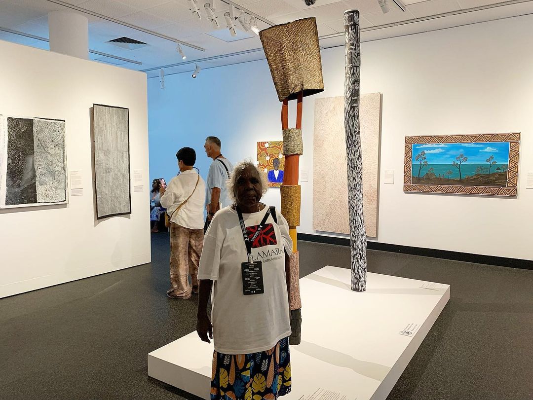 Kaye Brown stands at the Museum and Art Gallery of the Northern Territory with her ironwood tutini and bark tunga.