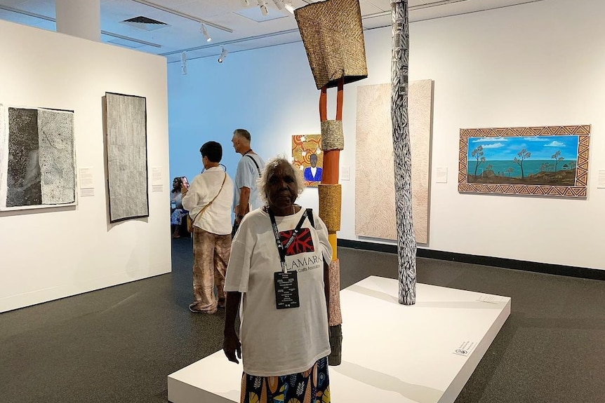 Kaye Brown stands at the Museum and Art Gallery of the Northern Territory with her ironwood tutini and bark tunga.