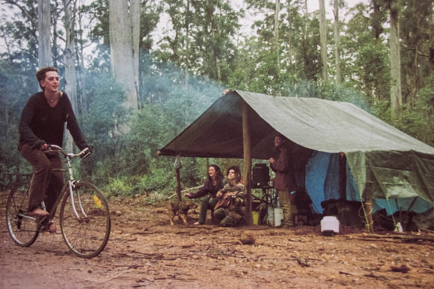 Old picture of woman riding a bicycle through a campsite while her friends look on 