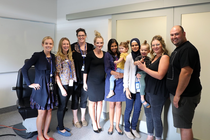 Ten people in a white room standing side by side