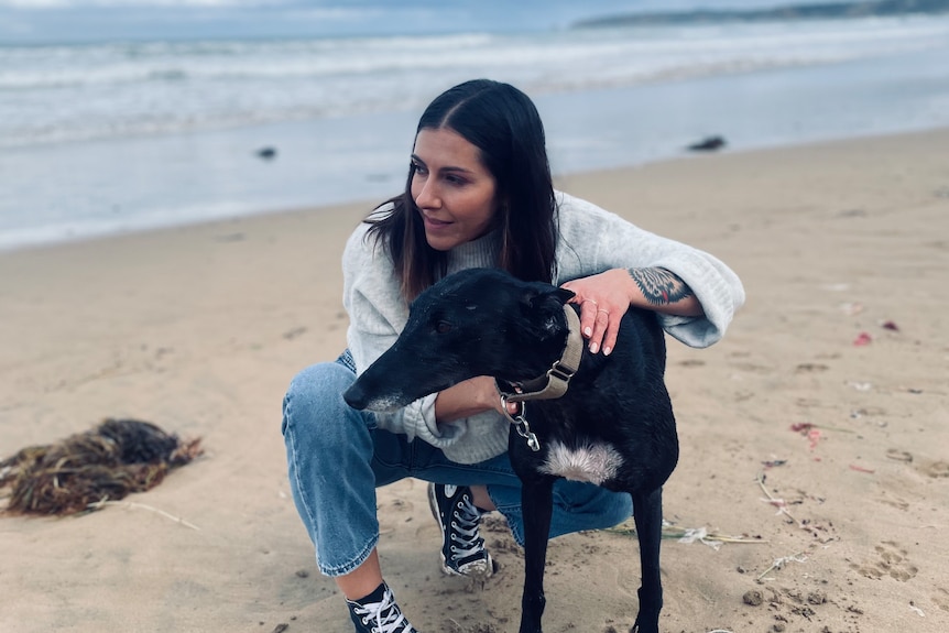 A woman on a beach with a greyhound
