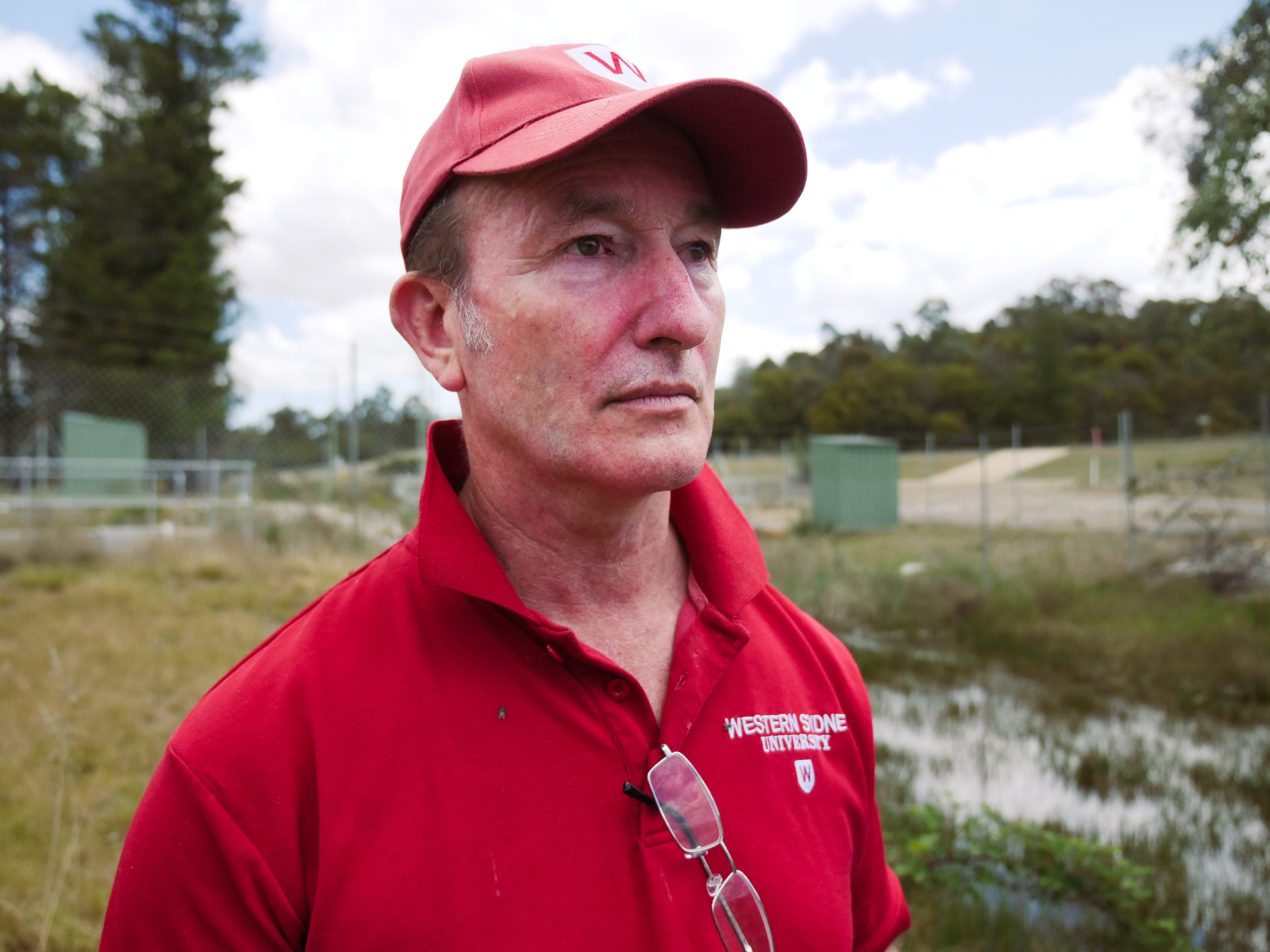 Man in red t-shirt tests water at a green creek with a cup on a long pole