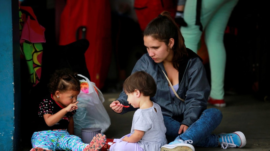 A woman is seen feeding children as they wait to cross the border.