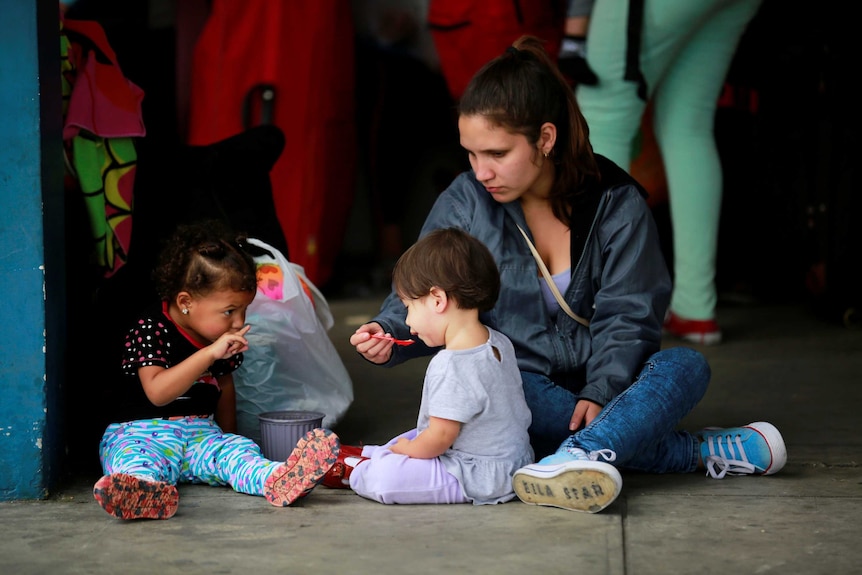 A woman is seen feeding children as they wait to cross the border.