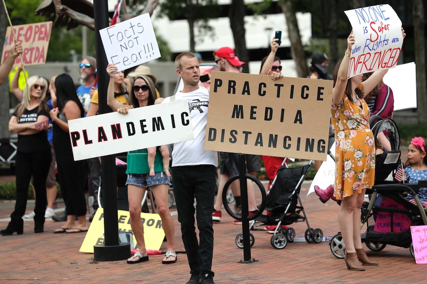 A group of protesters with signs reading "plandemic" and "pratice media distancing"