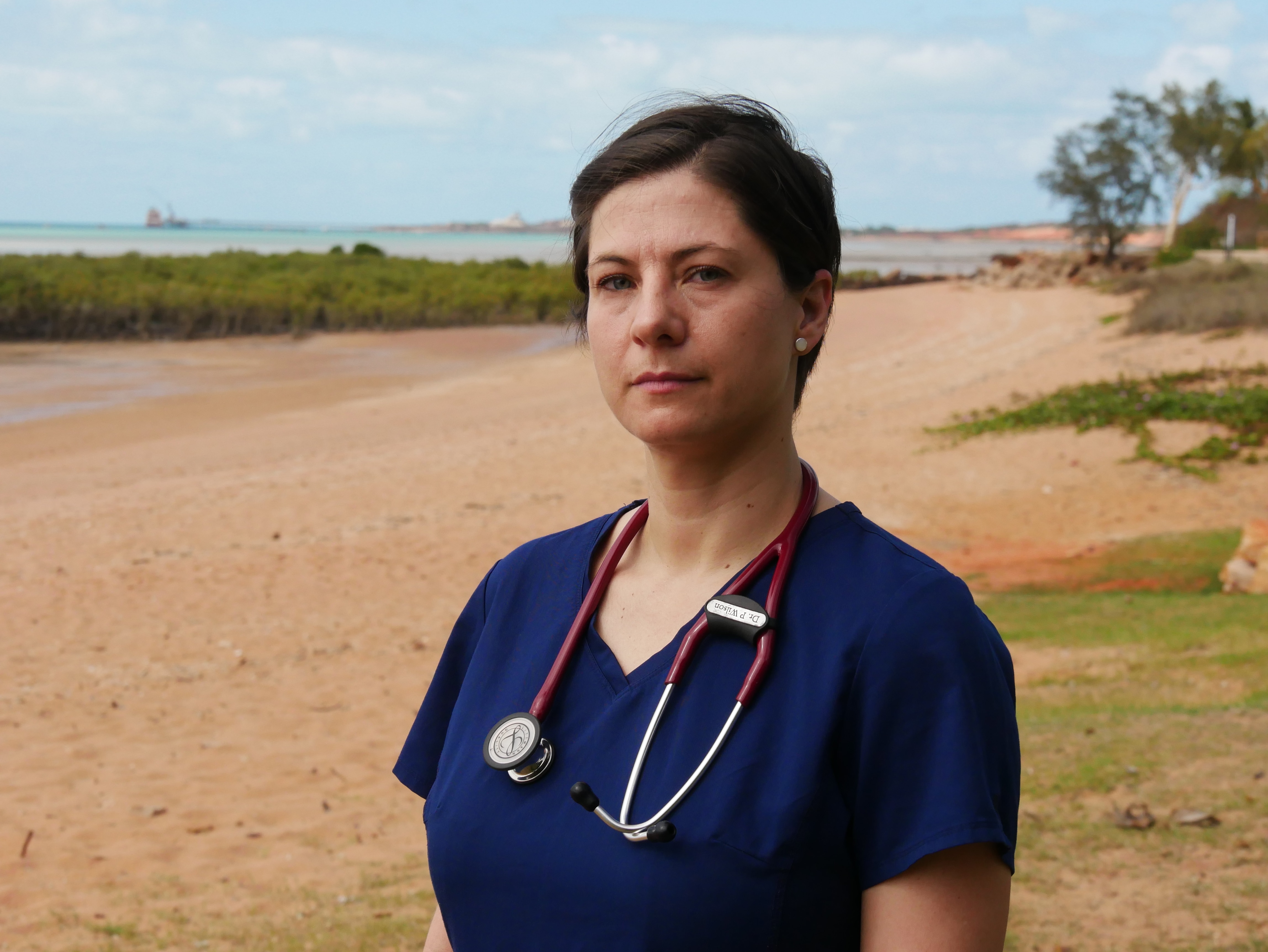 A woman standing on a beach with a stethoscope around her neck.