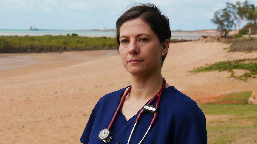 A woman standing on a beach with a stethoscope around her neck.