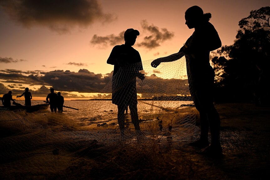 silhouettes of a family fishing on a shore are seen at sunset