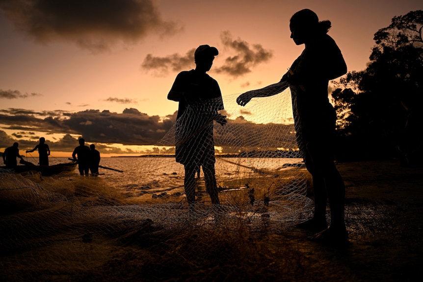 silhouettes of a family fishing on a shore are seen at sunset