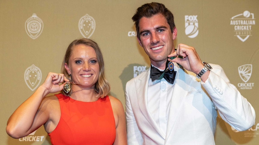 Alyssa Healy in a red dress, and Pat Cummins, in a white tuxedo, stand holding medals