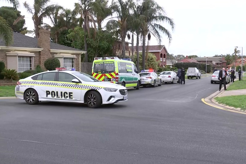 A police car parked across a small street with other police cars and an ambulance in it