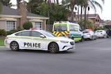 A police car parked across a small street with other police cars and an ambulance in it