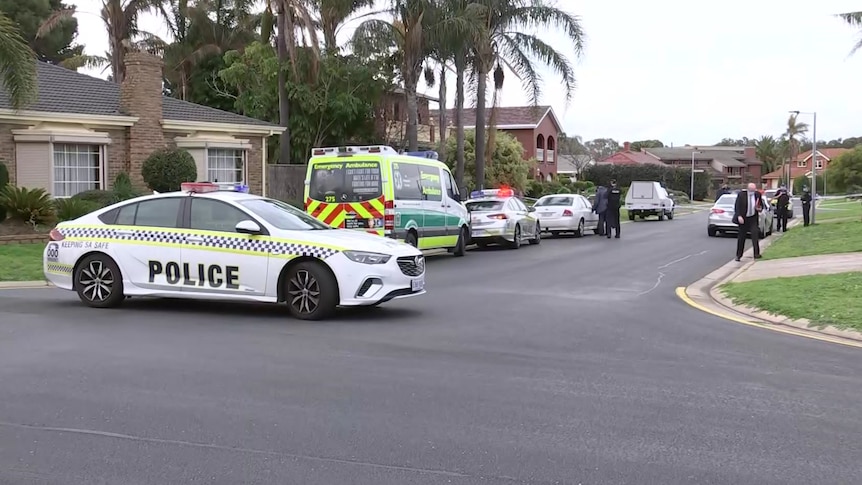 A police car parked across a small street with other police cars and an ambulance in it