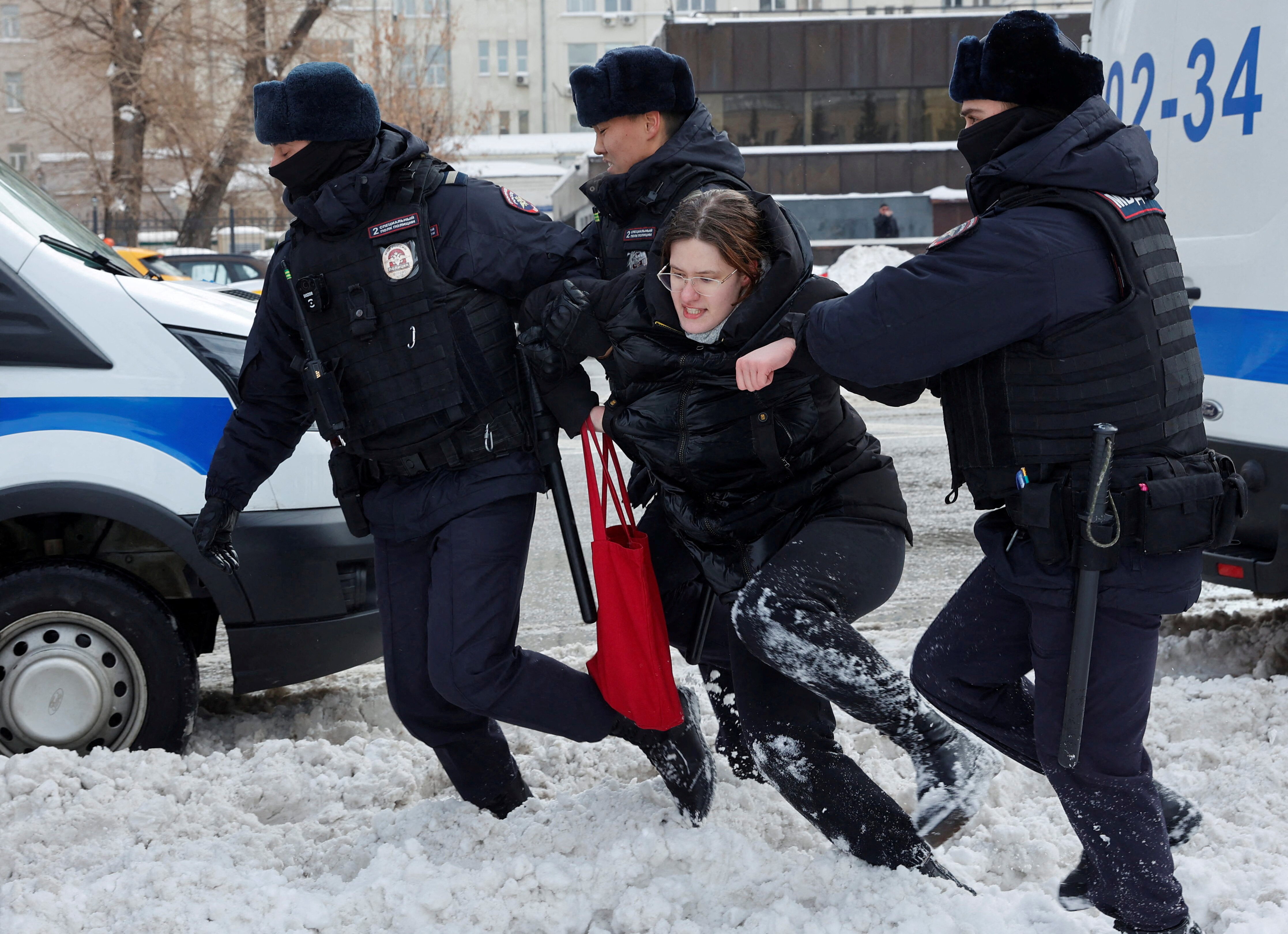 A woman wearing glasses stomps through the snow as three men hold her up.