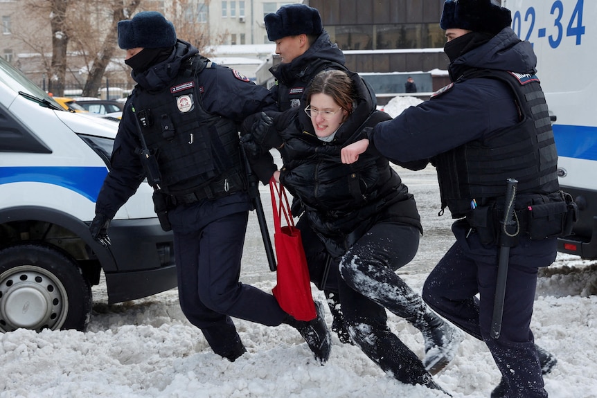 A woman wearing glasses stomps through the snow as three men hold her up.