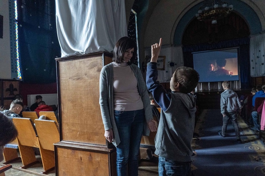 A woman looks down as a boy points in the air.