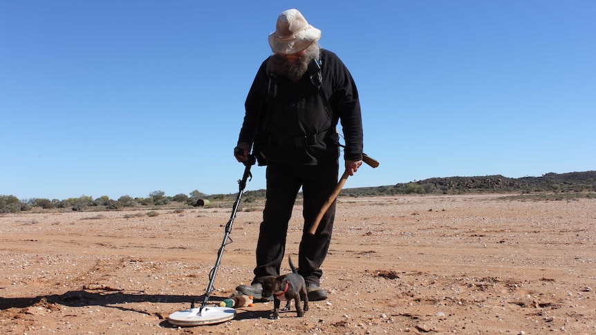 Landscape shot of Craig looking down to the red dirt with the puppy in between his legs