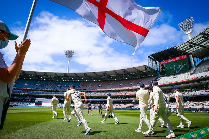 Cricket players run onto a pitch while England's flag flutters above them 