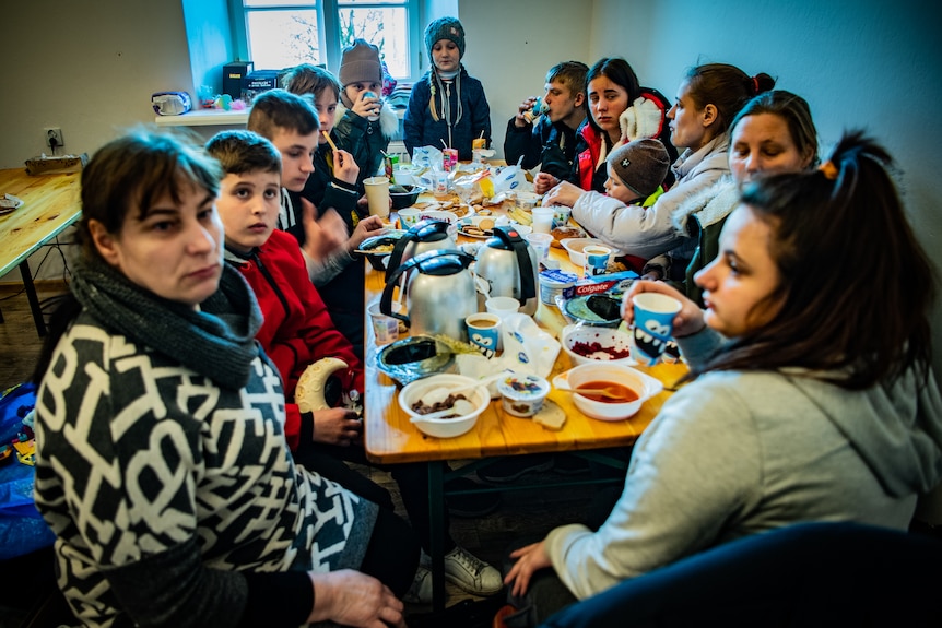 12 people gather around a long table to eat together. There are many children, and a couple of adults. 