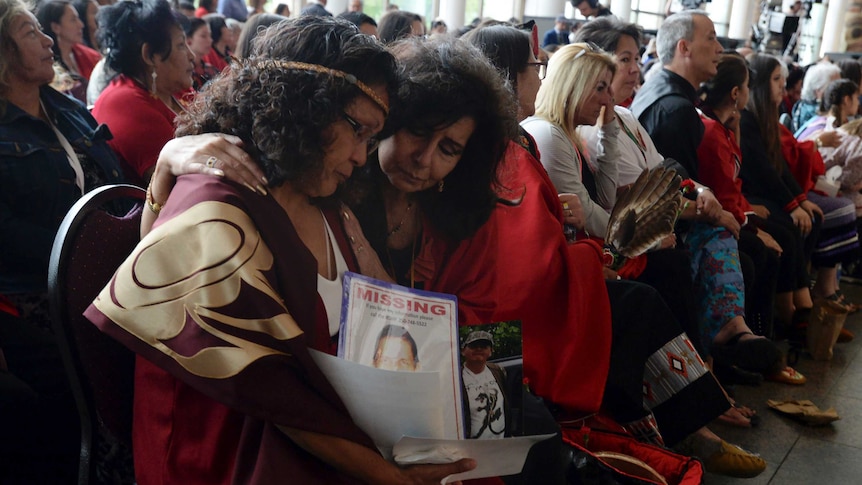 Attendees console each other while holding a photo, one of which says missing.