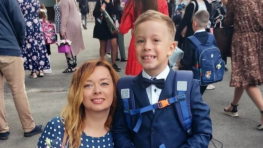 A woman holds flowers as she smiles next to a young boy in school uniform.