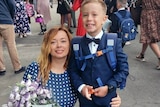 A woman holds flowers as she smiles next to a young boy in school uniform.