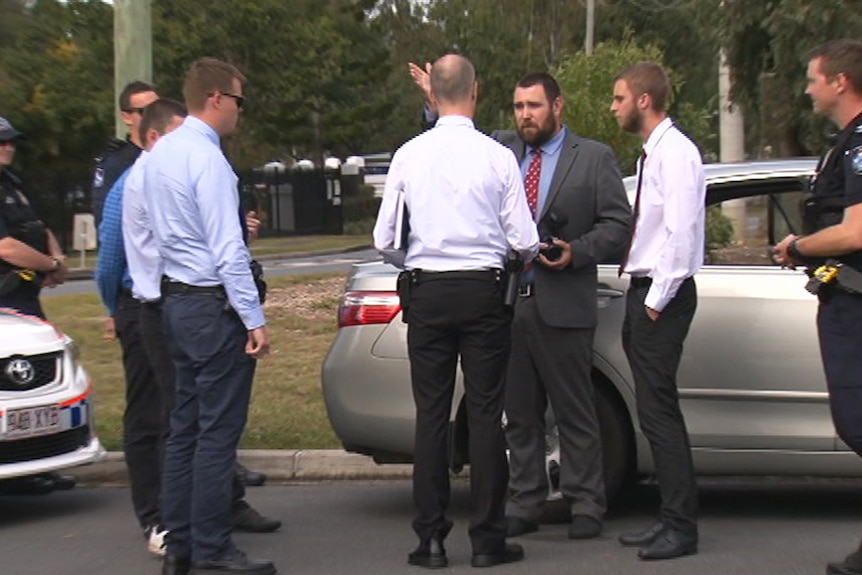 Detectives speaking to a group of men on the side of the road