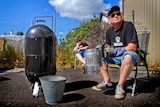 A man and woman sit outdoors by a barbecue smoker